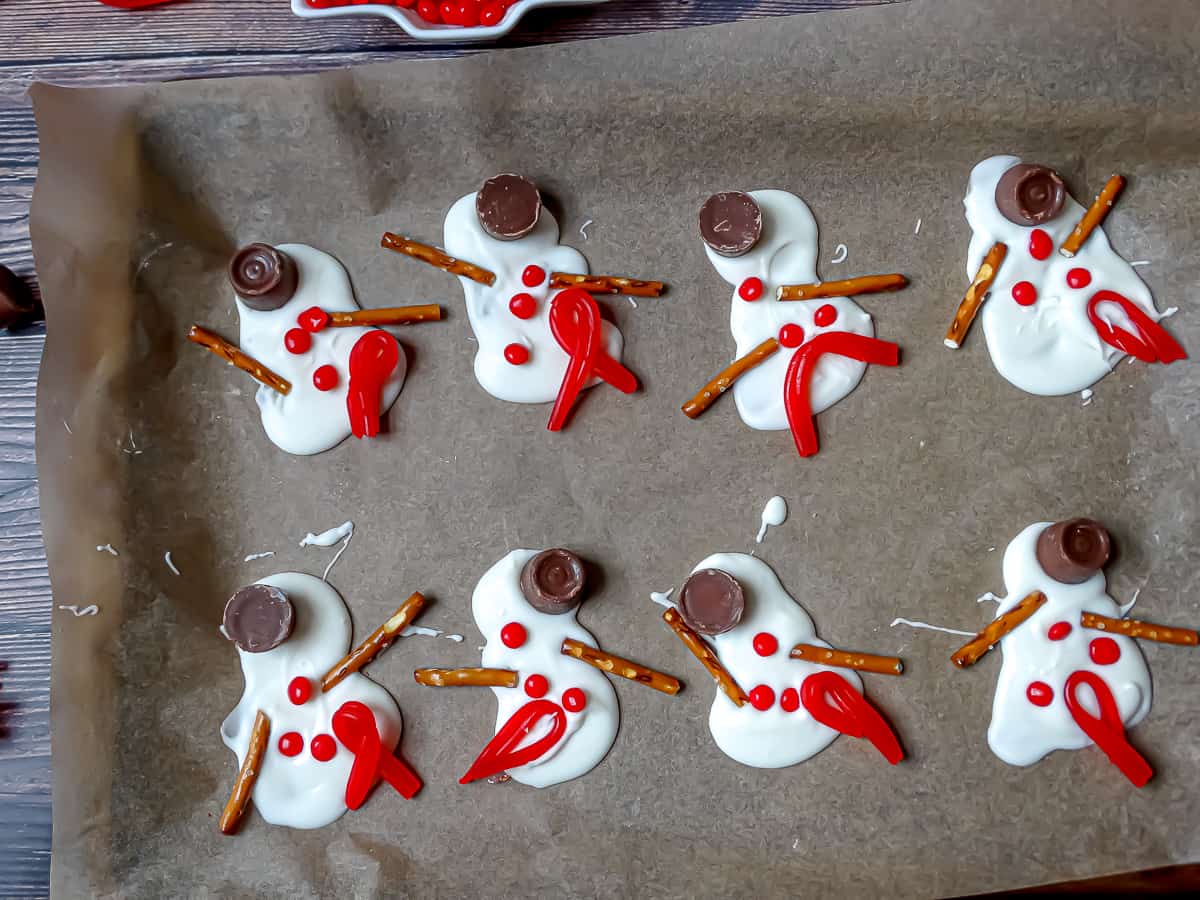 melted snowman with candy hats, scarves, buttons and arms on a piece of parchment paper