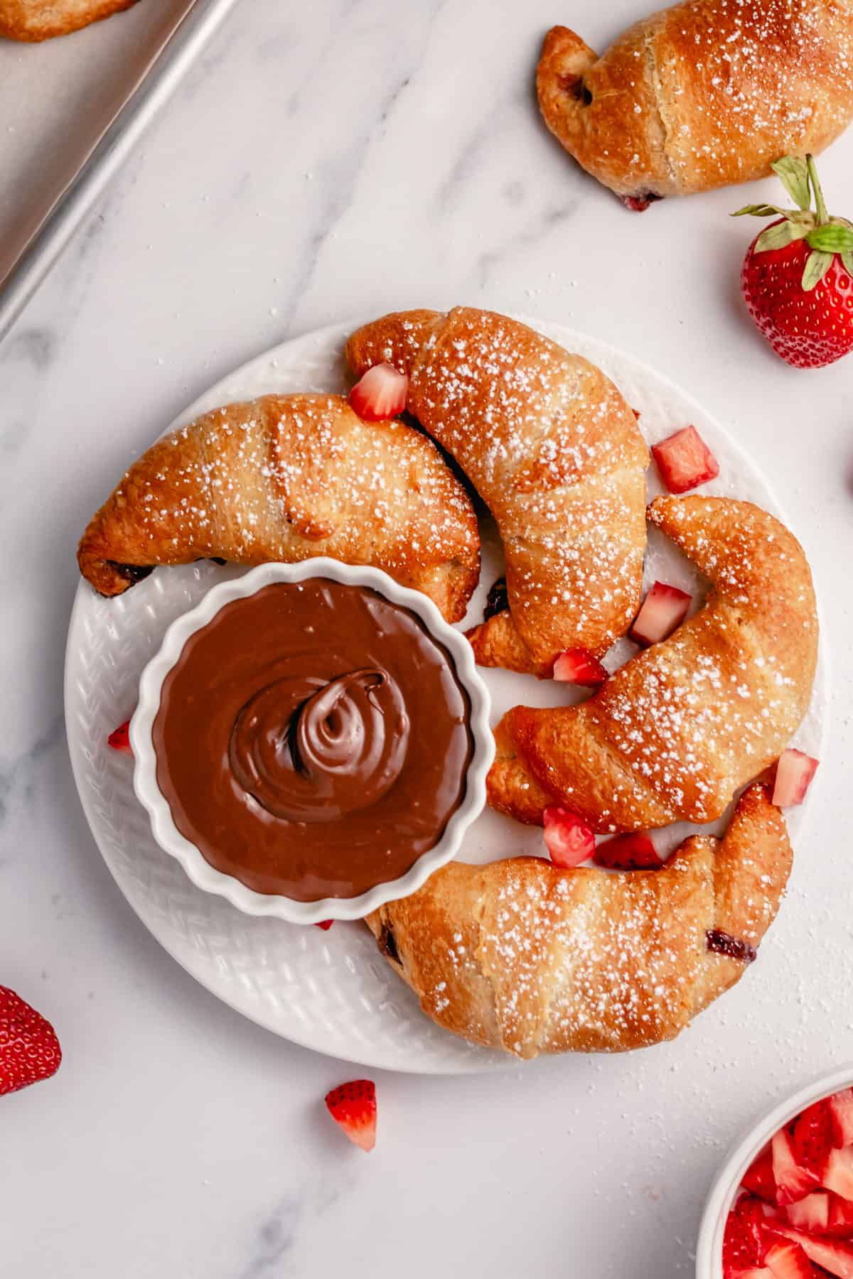 nutella crescent rolls surrounded by strawberry slices on a white serving plate