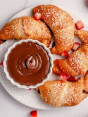 strawberry and nutella stuffed crescent rolls on a white plate sprinkled with powdered sugar