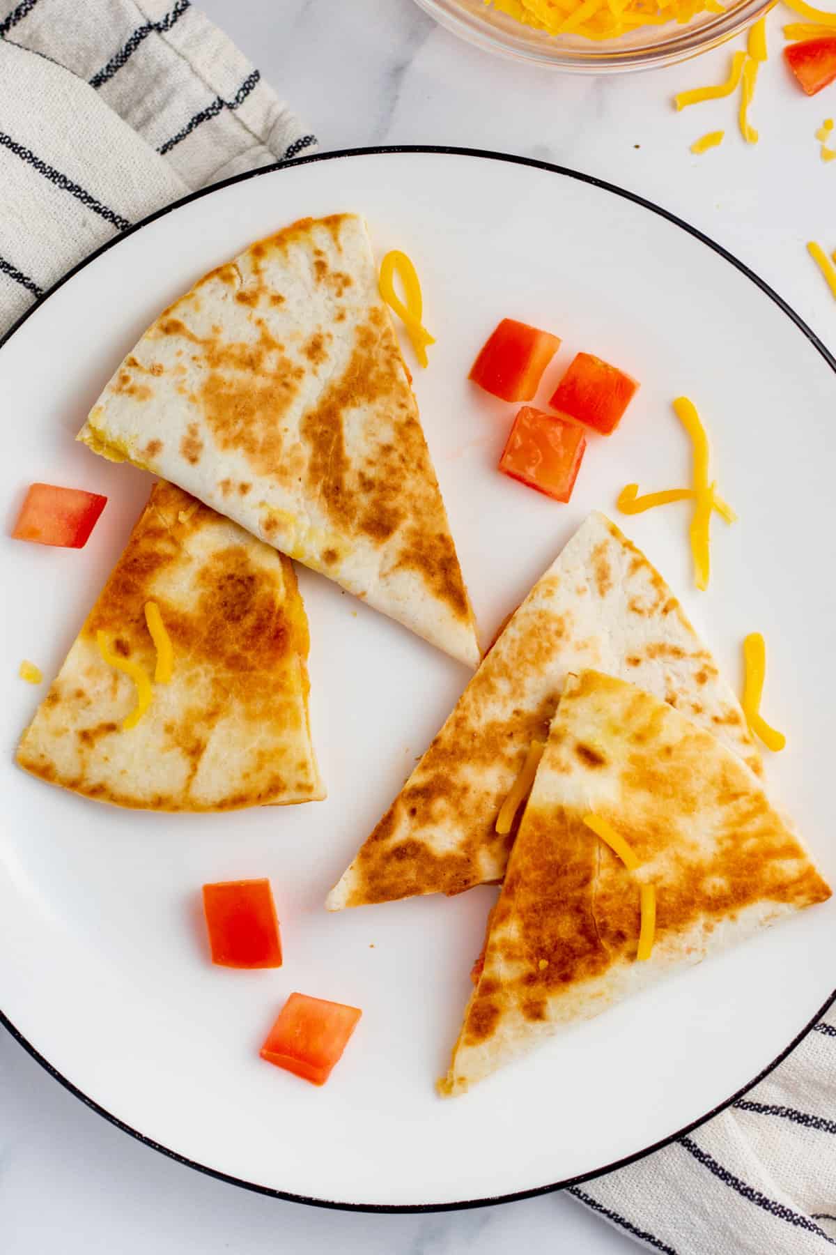 sliced cheese quesadilla on a white plate surrounded by tomatoes