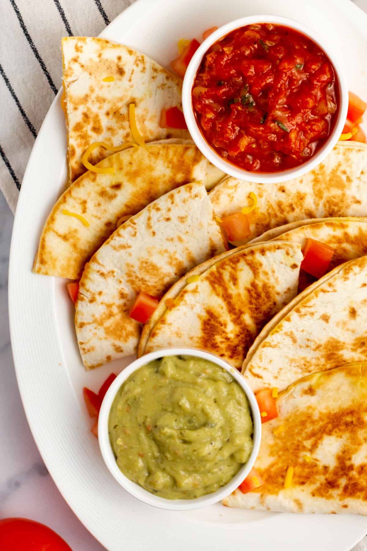 cheese quesadilla cut into slices on a white plate with guacamole and salsa