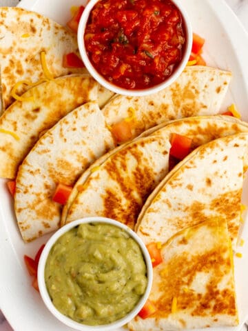 cheese quesadilla cut into slices on a white plate with guacamole and salsa