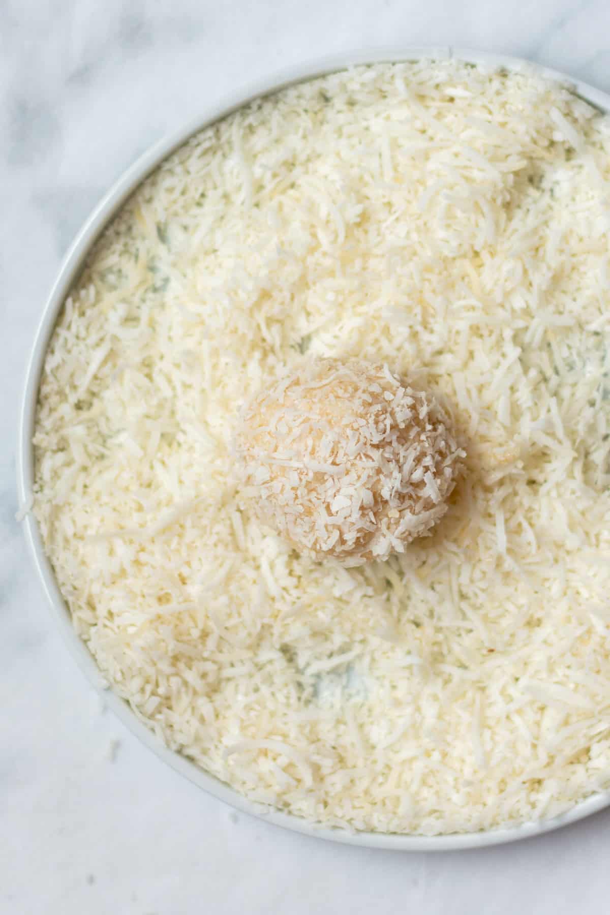 no bake cheesecake bite being rolled in shredded coconut