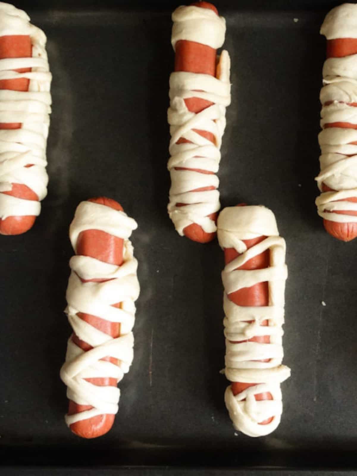uncooked mummy hot dogs on a baking sheet
