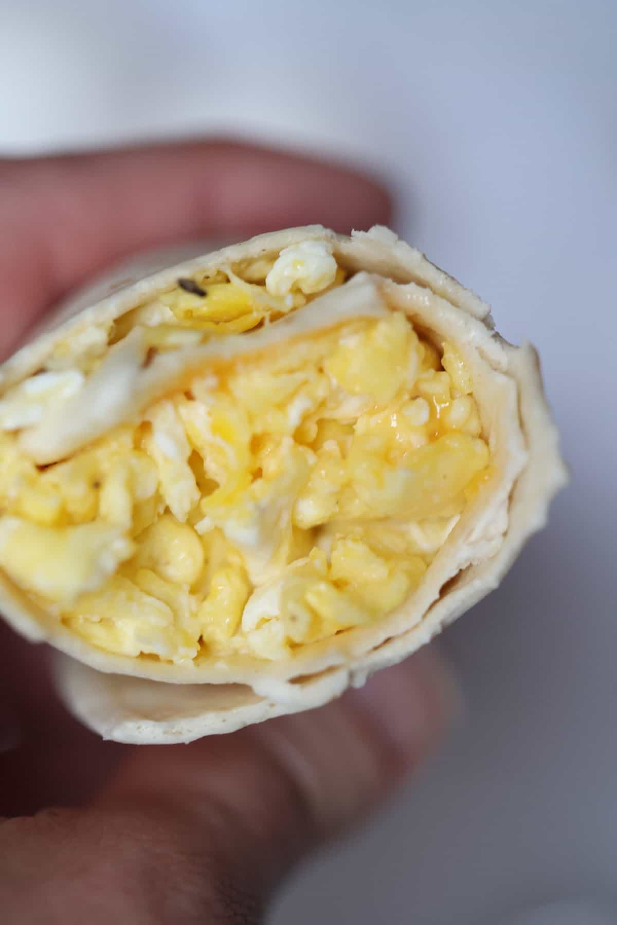 breakfast burrito with egg and cheese held in a hand