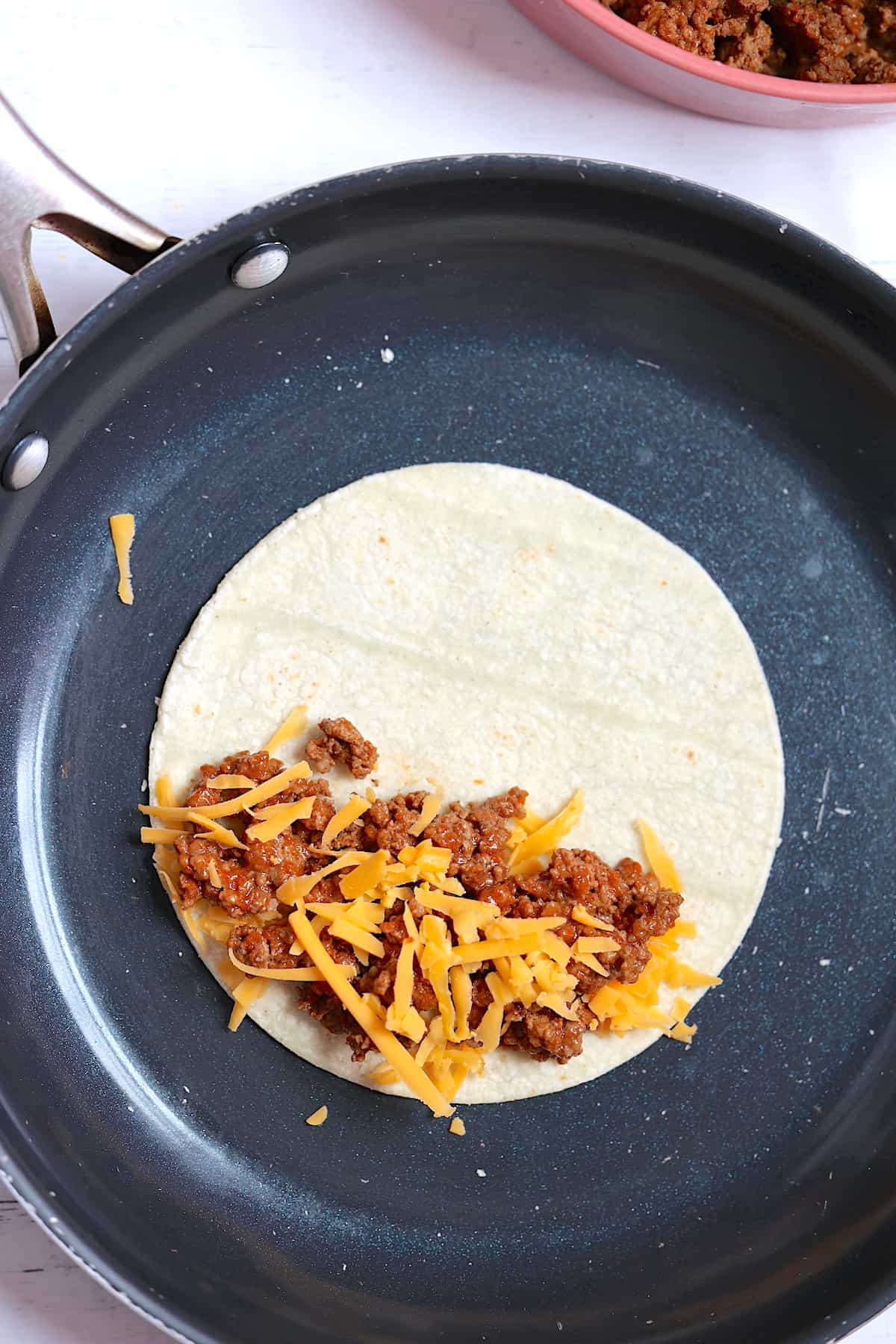 ground beef and cheese on a corn tortilla in a frying pan