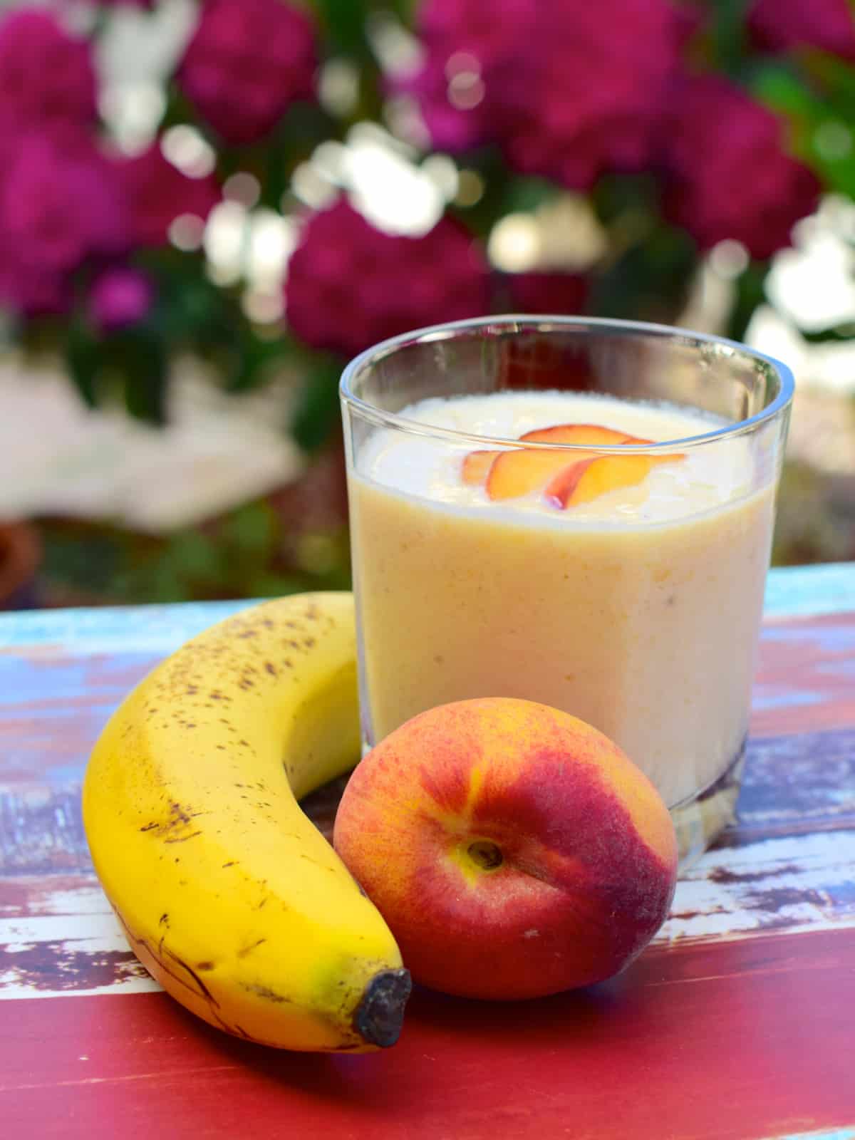 banana peach smoothie in a glass cup garnished fresh peach pieces
