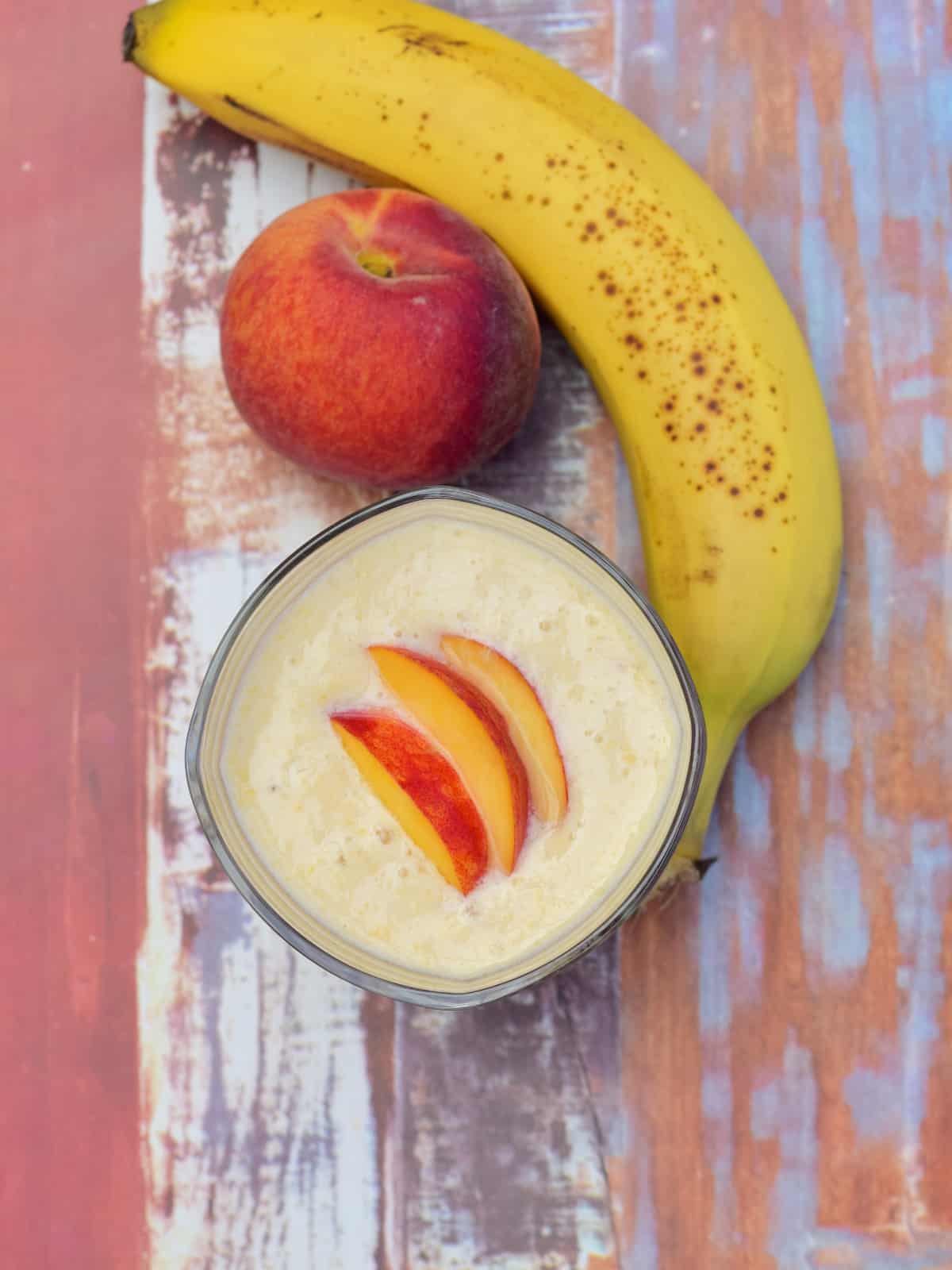 banana peach smoothie in a glass cup garnished fresh peach pieces