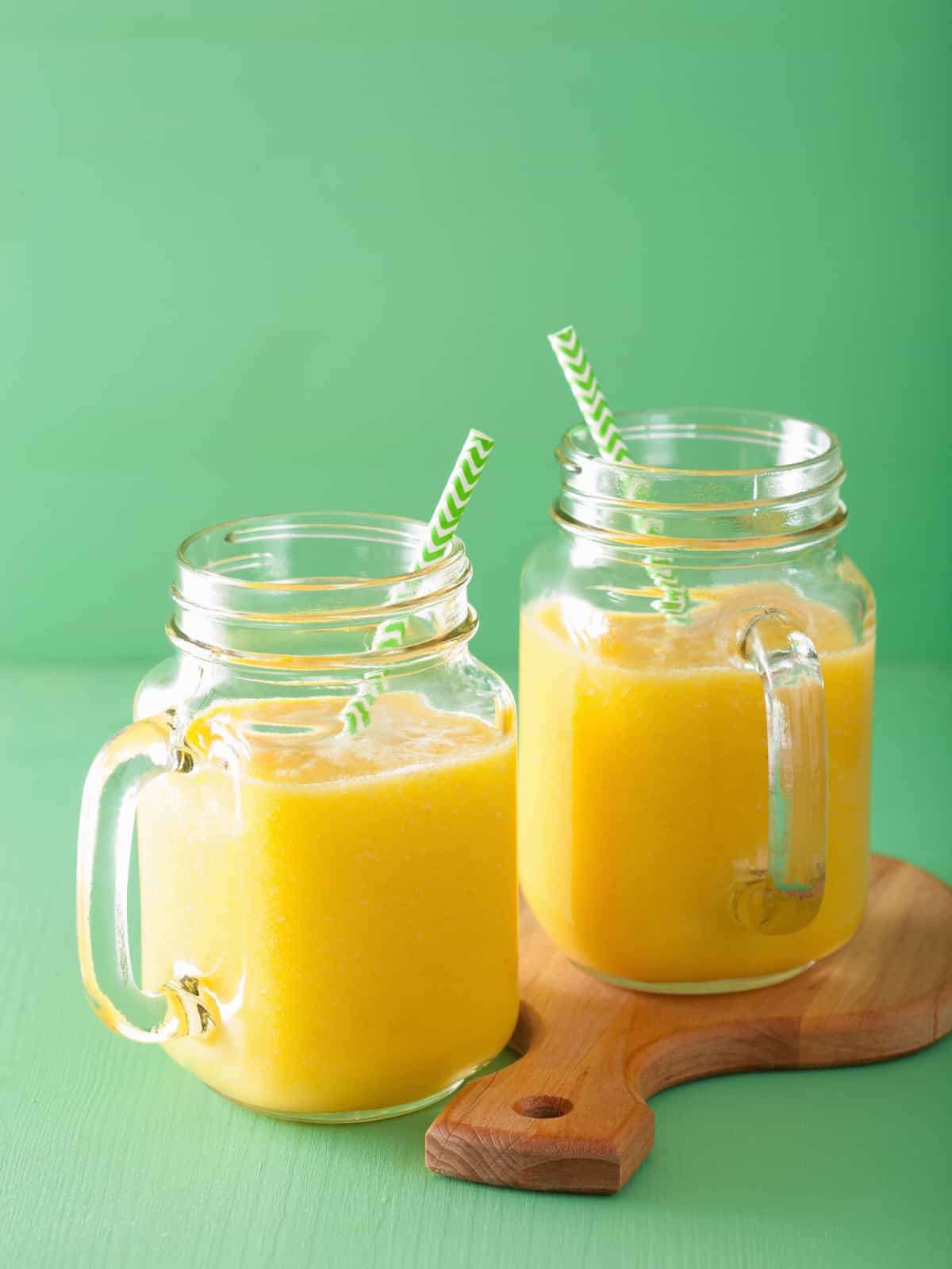 orange mango smoothie in 2 mason jars with a green background