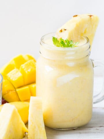 mango pineapple smoothie in a mason jar with pineapple slices and mango
