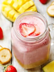 mango strawberry banana smoothie in a glass jar surrounded by fresh fruit