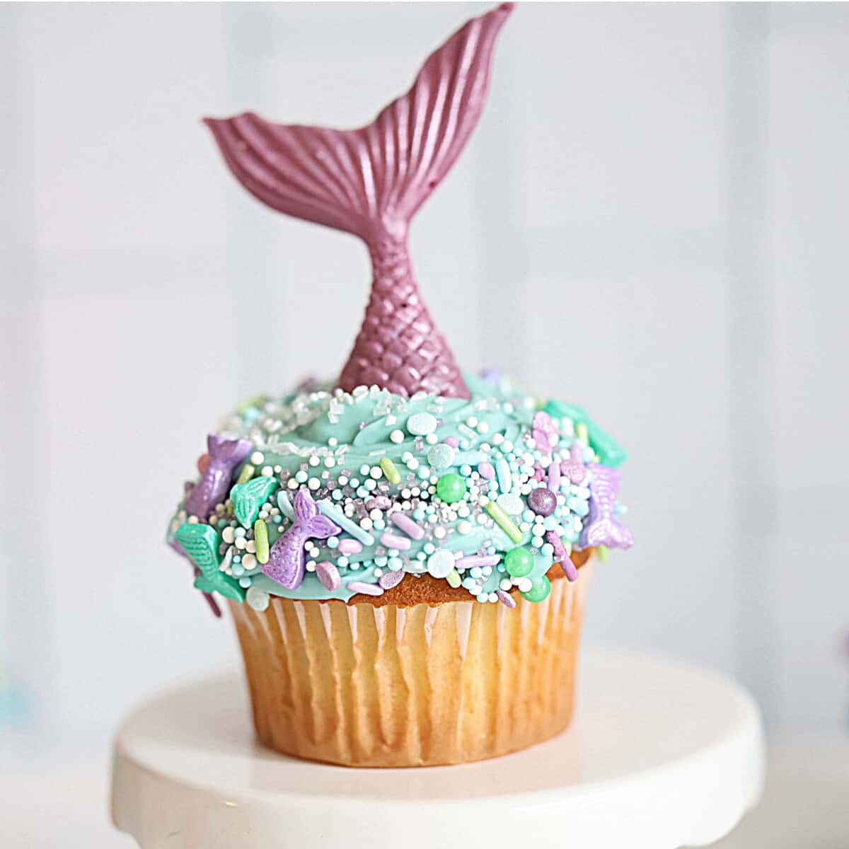 a cupcake with blue icing, mermaid sprinkles, and a mermaid tail on top