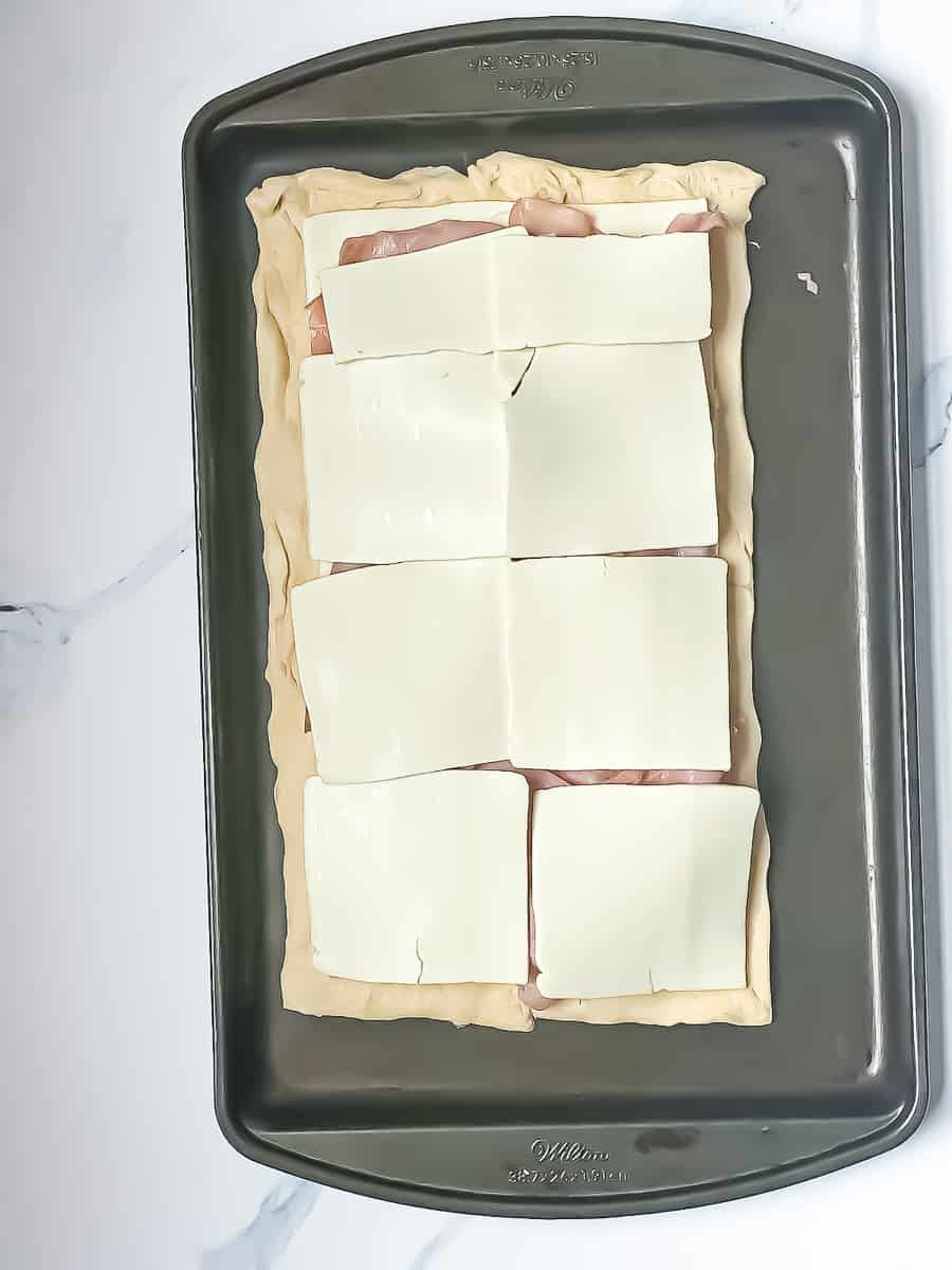 crescent dough on a baking sheet topped with ham and cheese