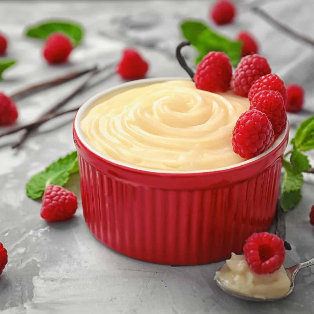 vanilla pudding in a red ramekin topped with raspberries