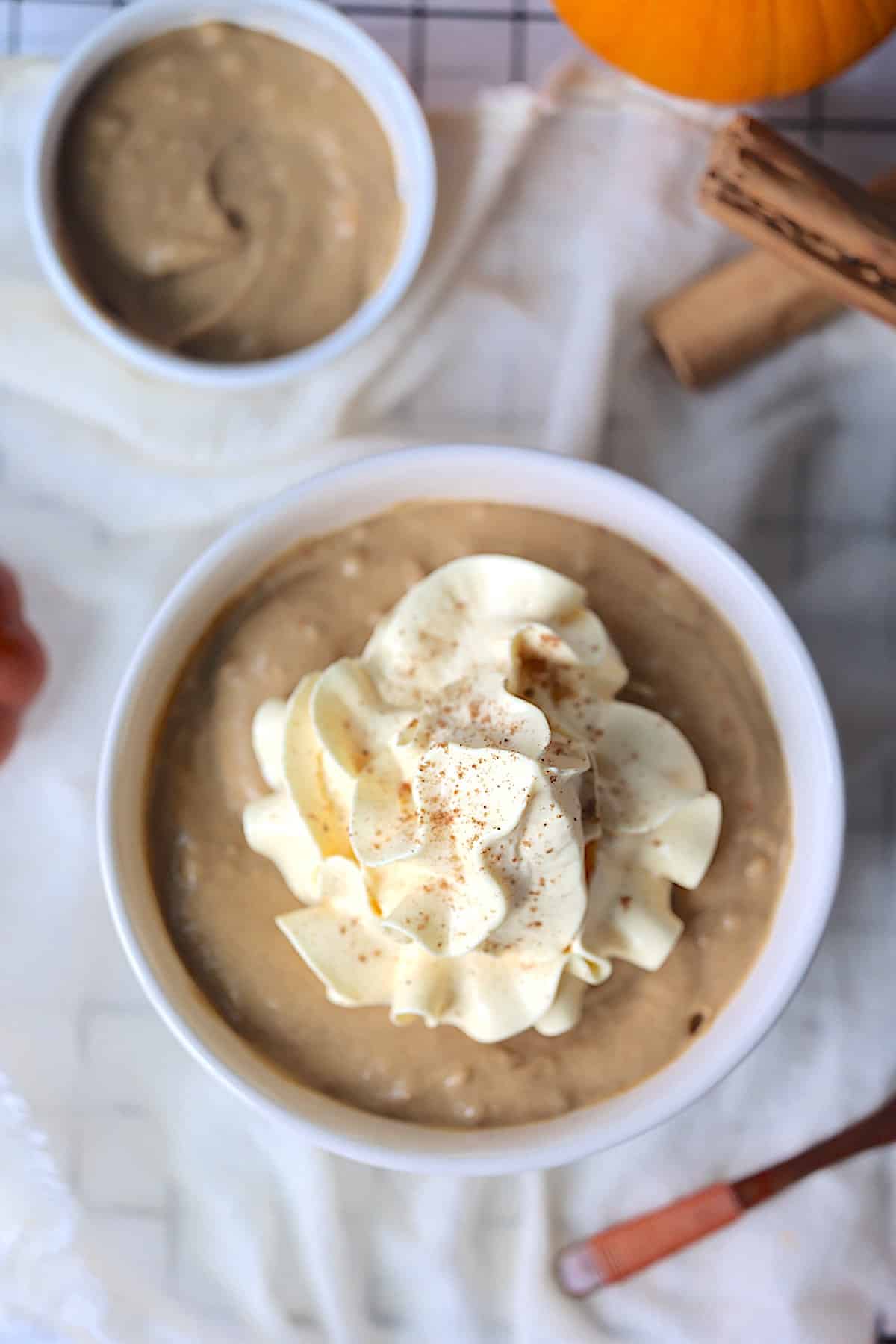 vegan pumpkin pudding in a white bowl topped with whipped cream and nutmeg
