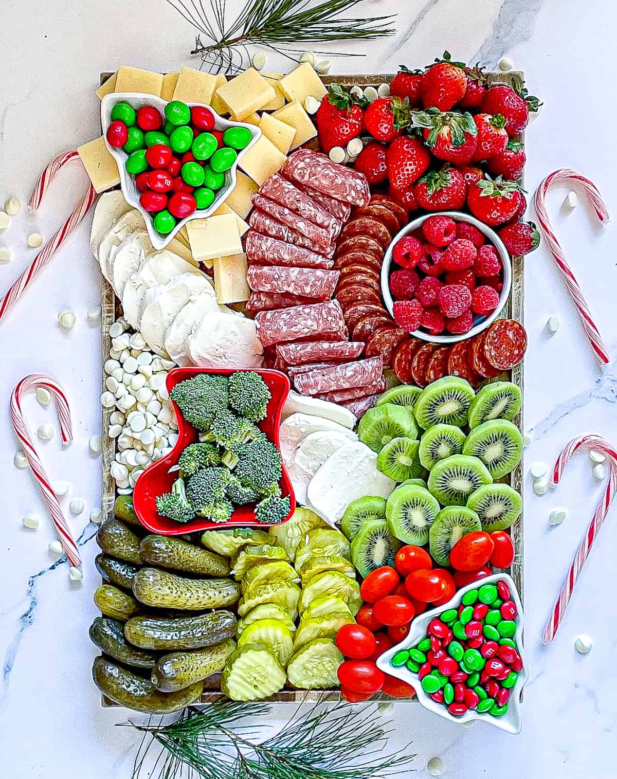 kids christmas charcuterie board surrounded with candy canes and full of red, green and white food
