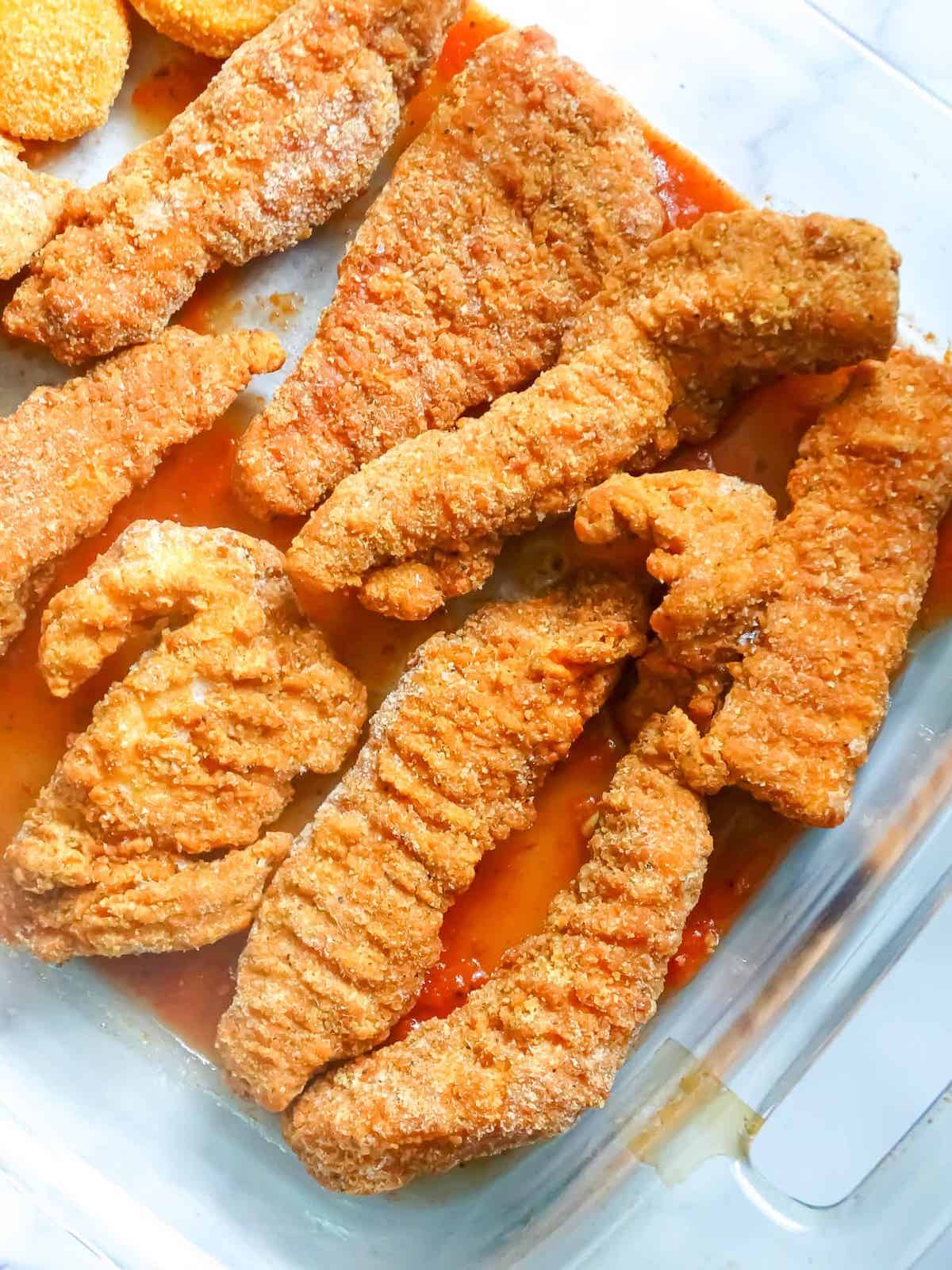 breaded chicken tenders and marinara sauce in a glass baking dish