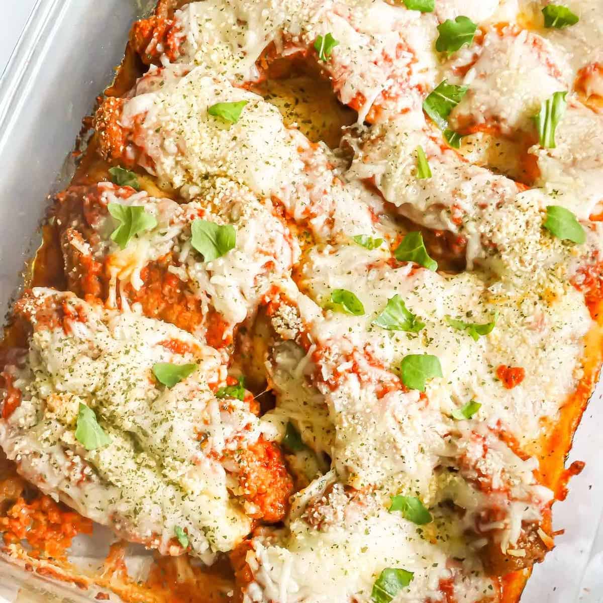 chicken tenders parmesan topped with cheese and herbs in a baking dish