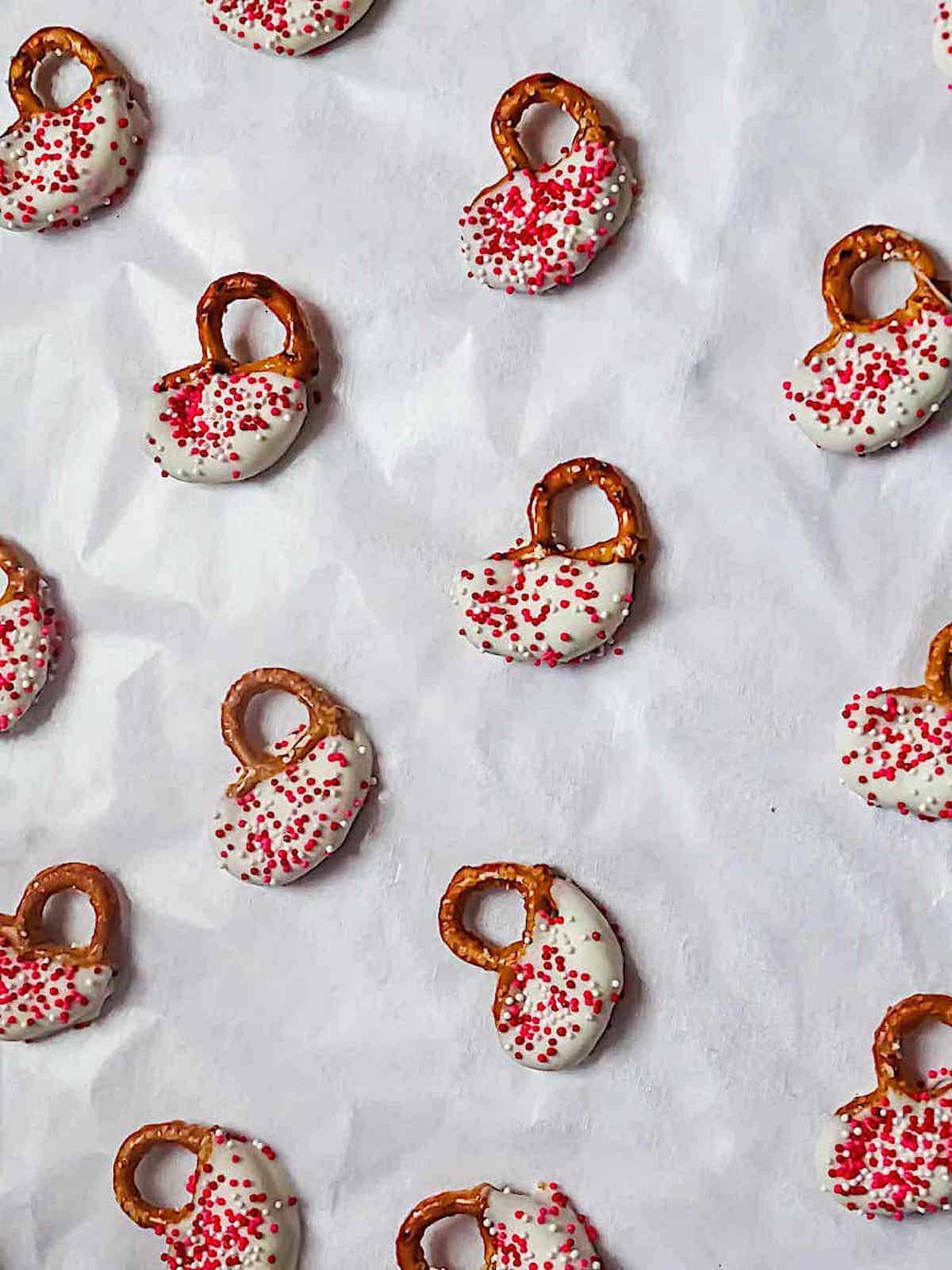 white chocolate covered mini pretzels decorated with pink sprinkles on parchment paper