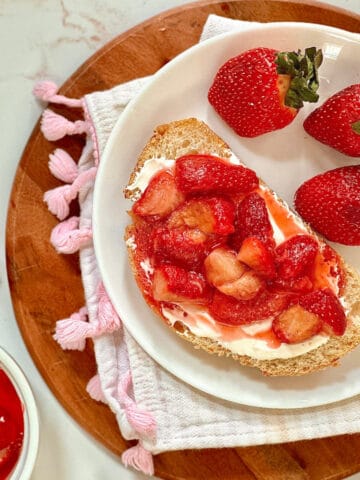 strawberry cream cheese toast on a white plate surrounded by fresh strawberries