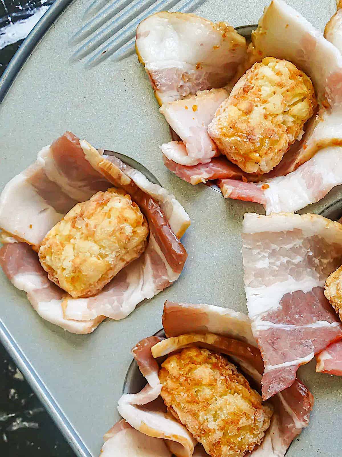 tater tots stuffed onto bacon slices in a muffin tin