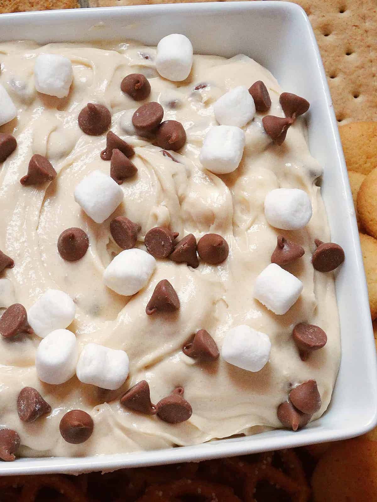 s'mores dip topped with chocolate chips and marshmallows in a white serving bowl