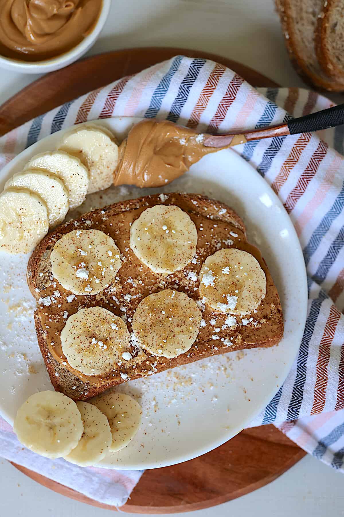 peanut butter banana toast on a white plate sprinkled with brown sugar and cinnamon
