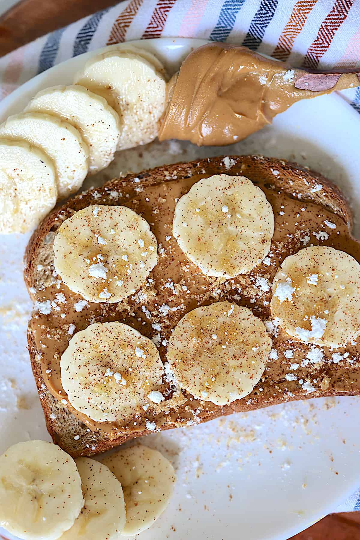 peanut butter banana toast on a white plate sprinkled with brown sugar and cinnamon