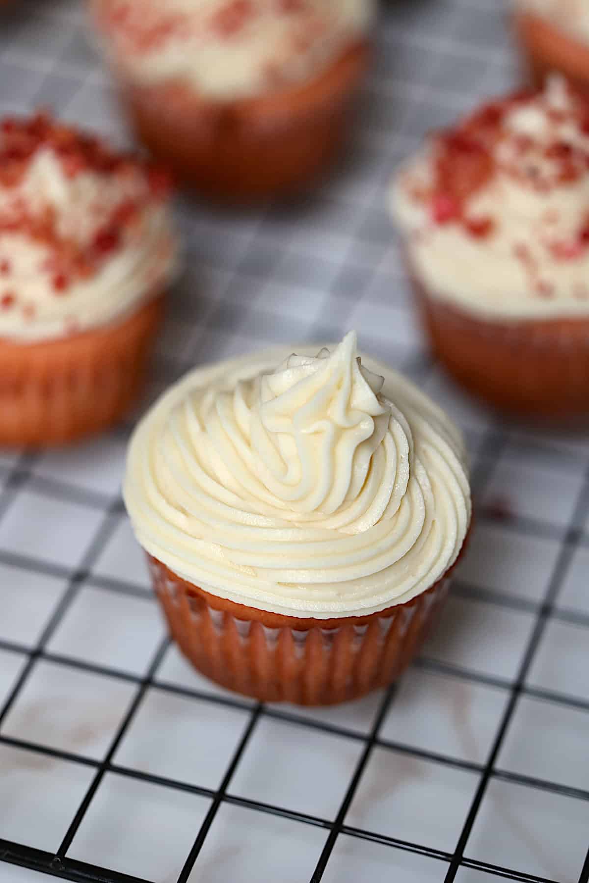 close up of a buttercream frosted cupcake on a cooling rack