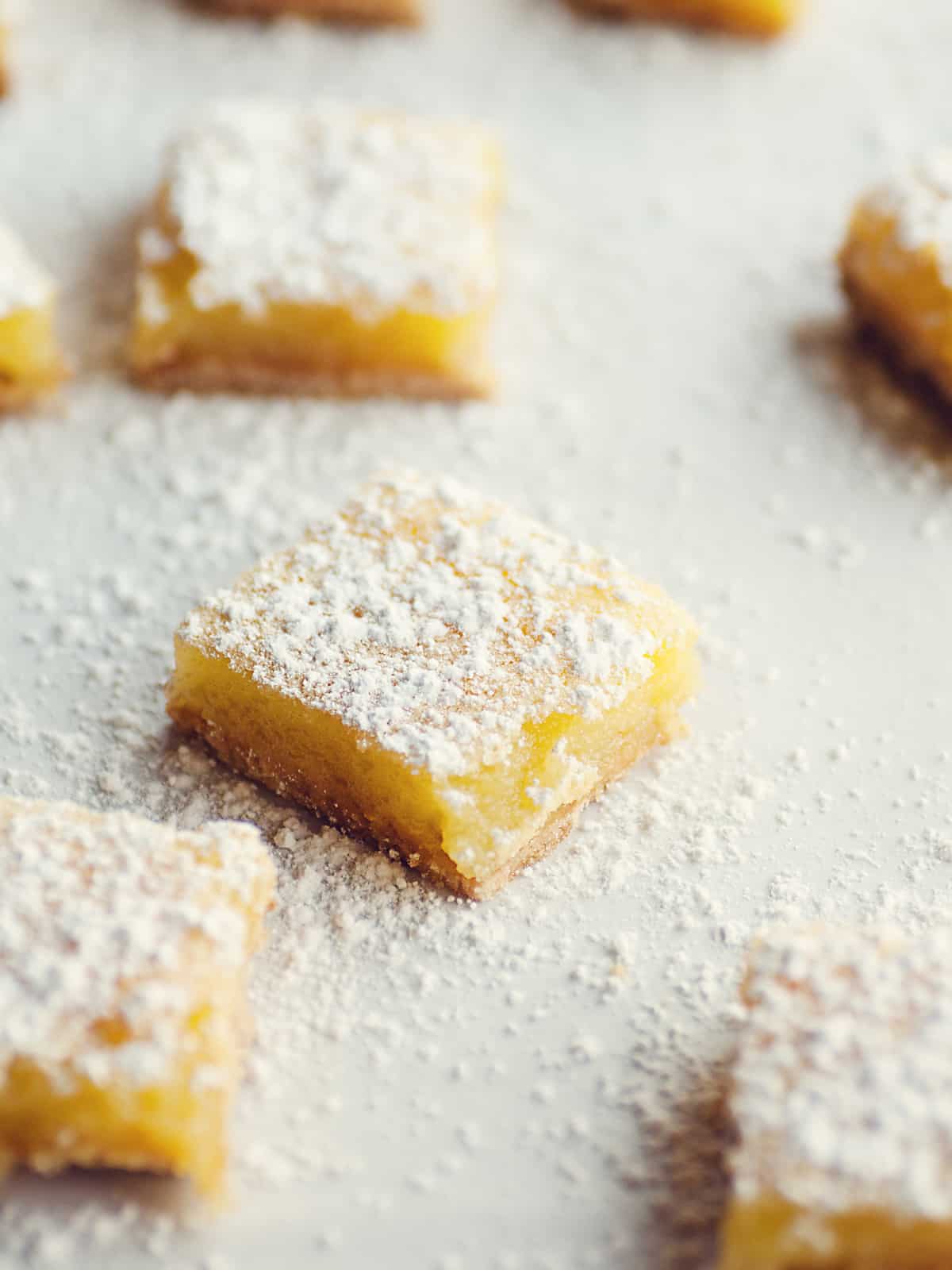 sliced creamy lemon bars on a parchment paper sprinkled with powdered sugar