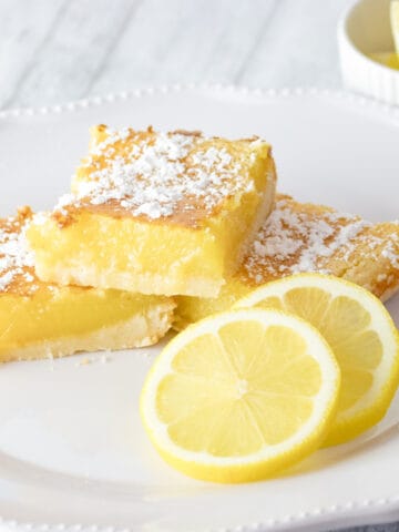 creamy lemon squares on a white plate with lemon slices