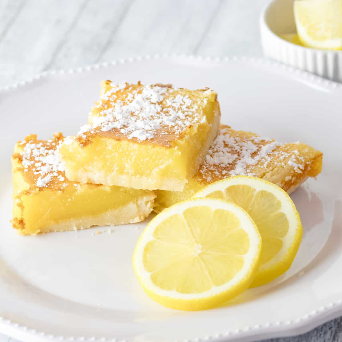 creamy lemon squares on a white plate with lemon slices