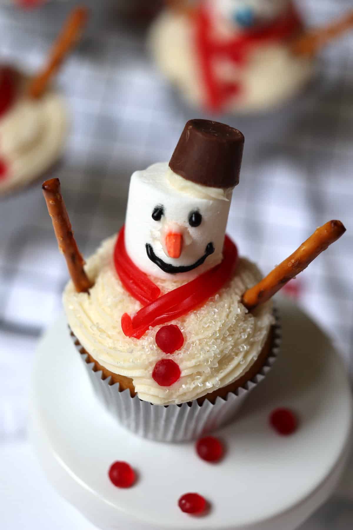 vanilla snowman cupcake topped with a marshmallow snowman on a cake plate
