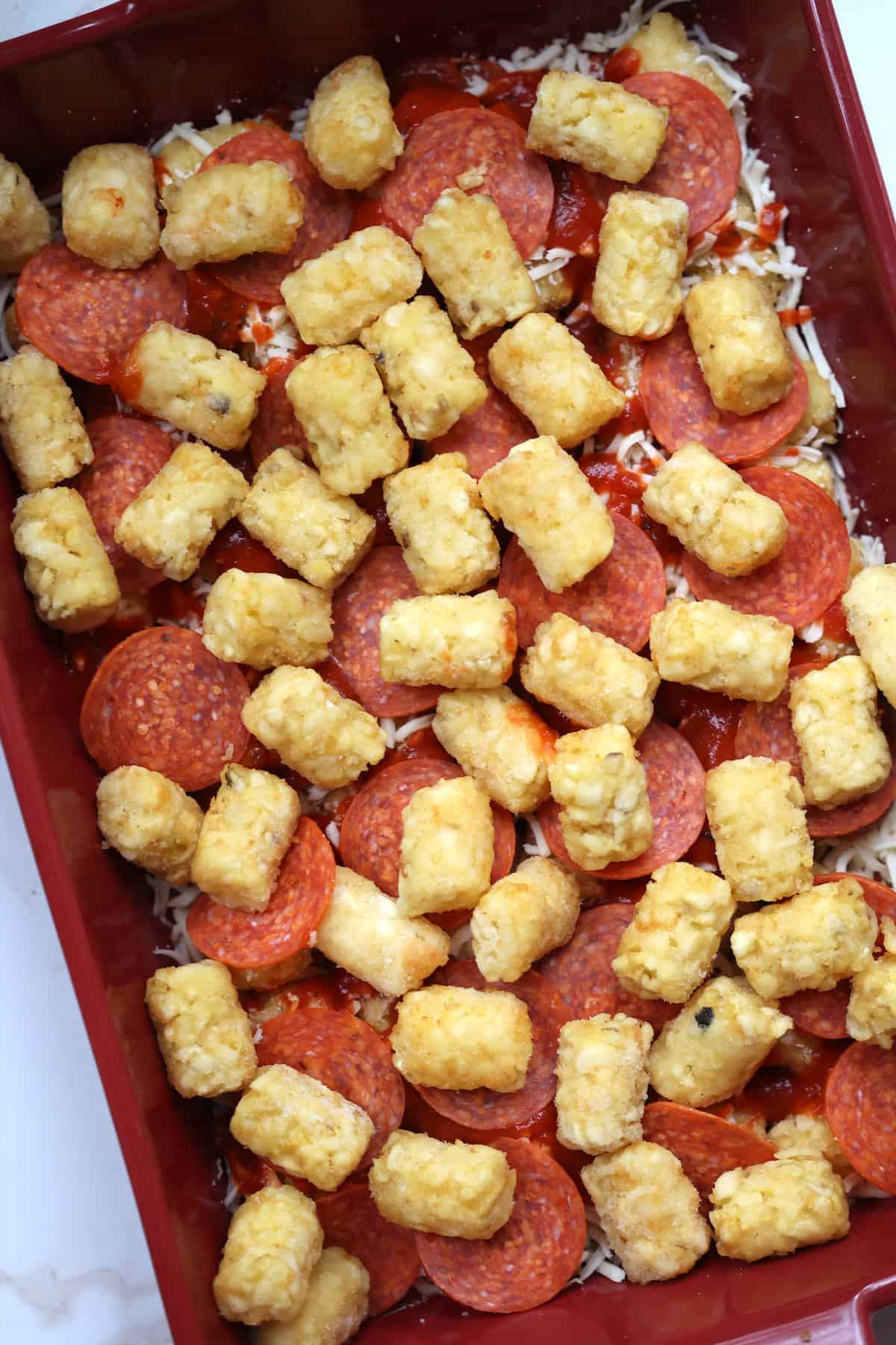 tater tots on top of pepperoni and pizza sauce in a casserole dish