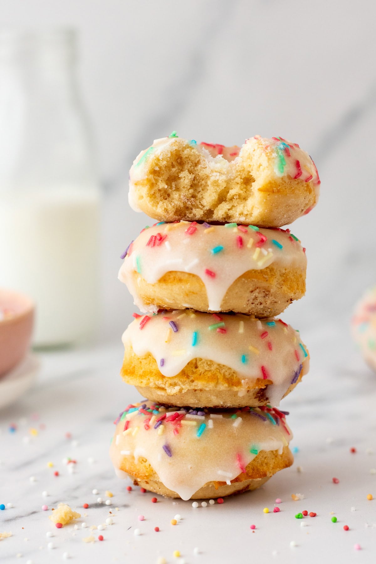 a stack of baked vanilla donuts with rainbow sprinkles and glaze