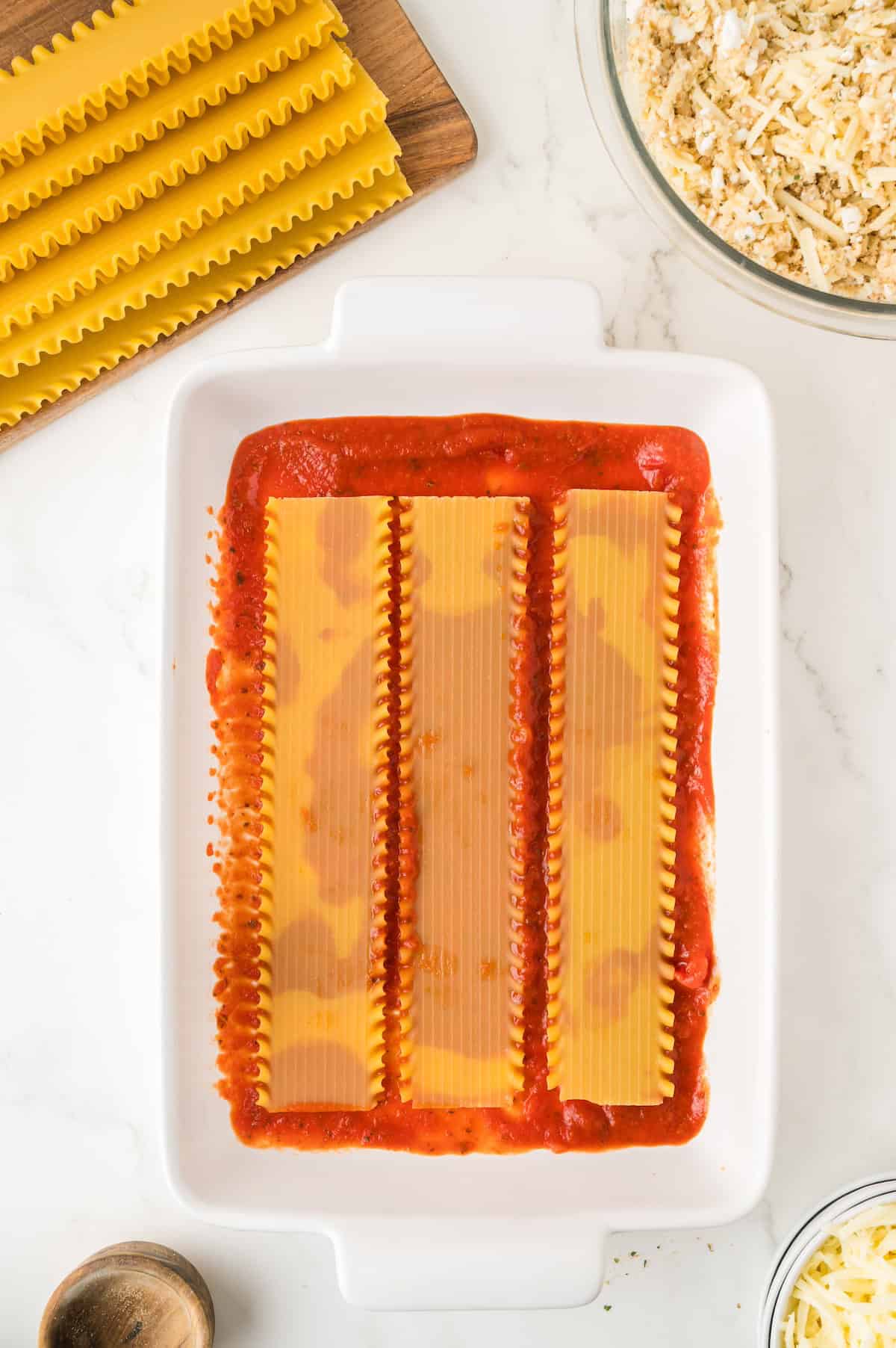 a layer of sauce and lasagna noodles in a baking dish
