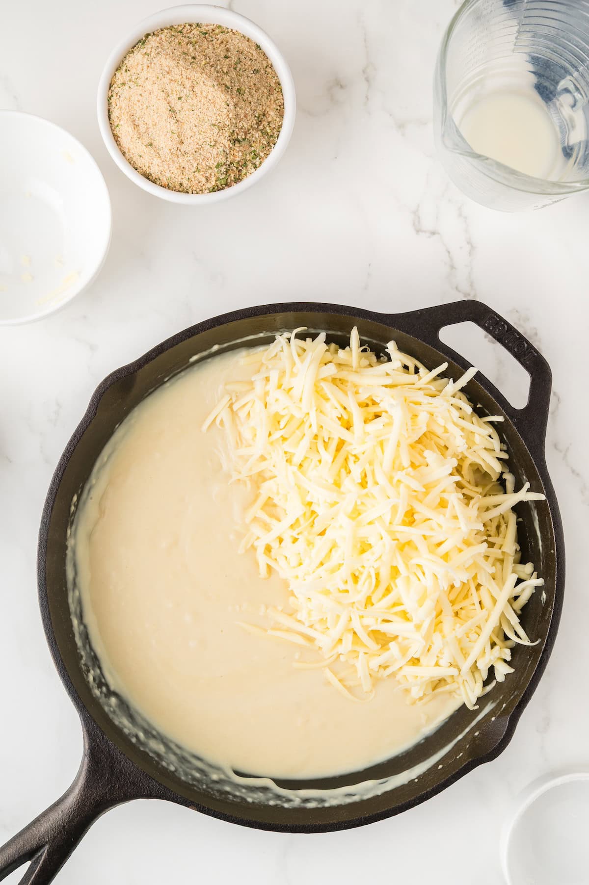 cheese and milk being put into a cast iron skillet