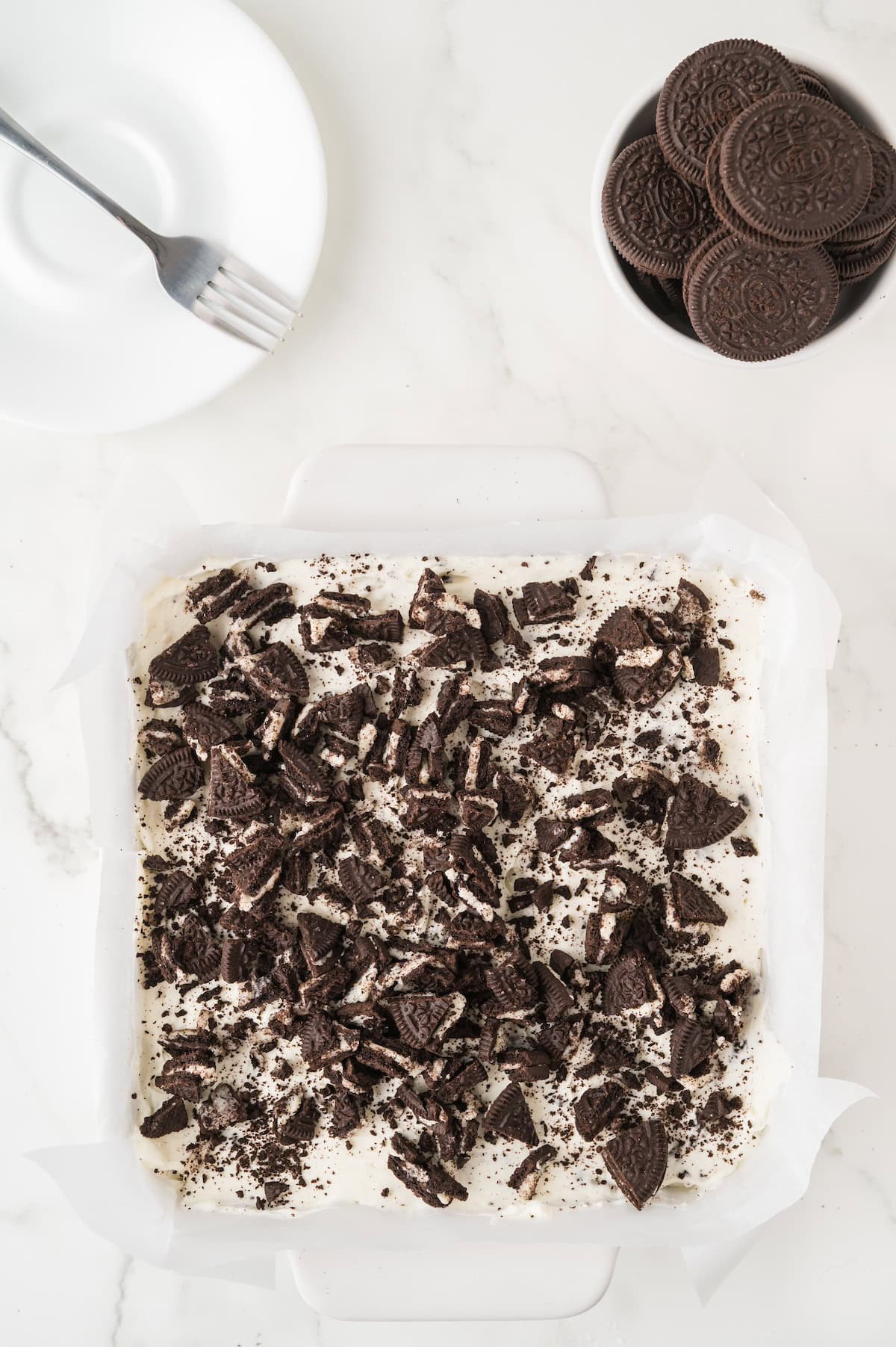 Oreo cheesecake filling in a baking dish topped with crumbled Oreos